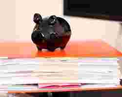 Ein Sparschwein sitzt auf einem Ordner voller Versicherungsunterlagen.