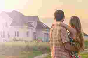 Ein Paar steht Arm in Arm mit dem Rücken zur Kamera und blickt auf ein Haus.