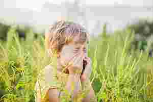 Ein kleiner Junge steht im Feld, ist von Gräsern umringt und muss nießen.